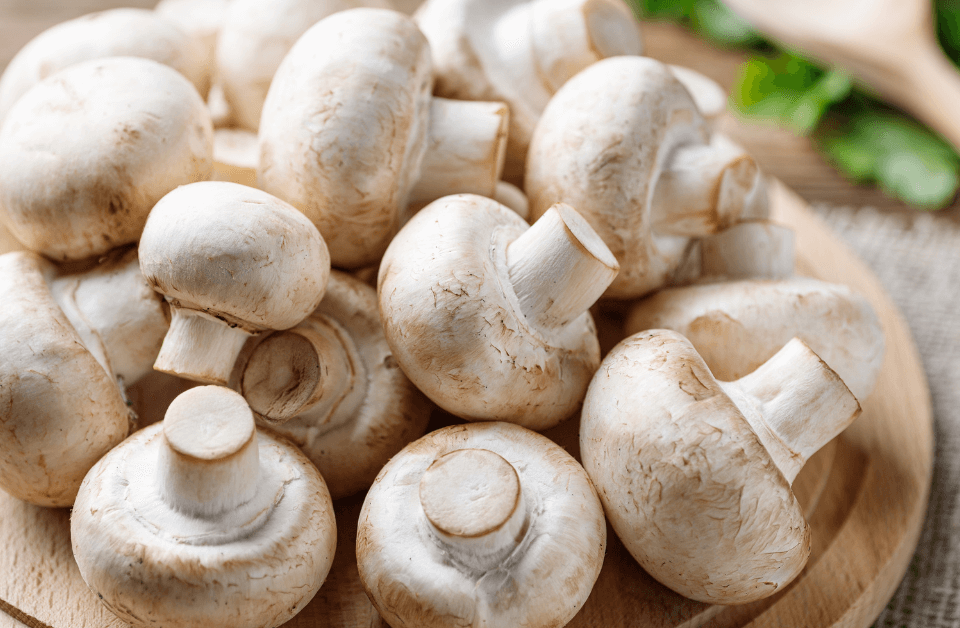 Tagliere di legno con coltello e funghi champignon