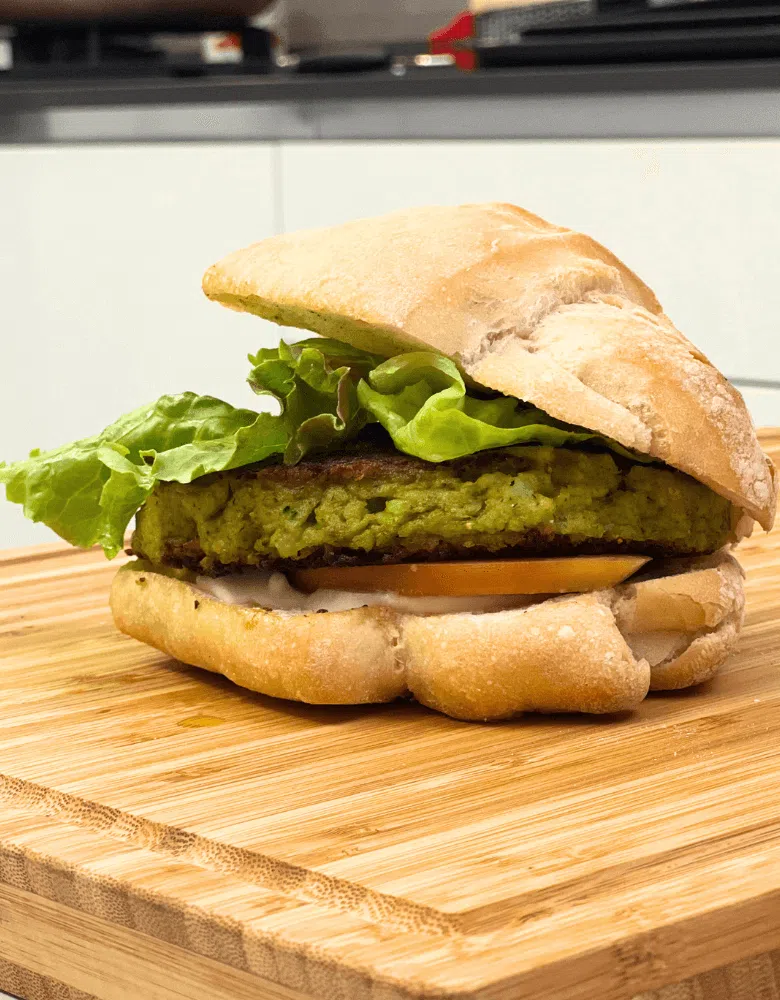 Panino con hamburger di broccolo, insalata a pomodoro su tagliere